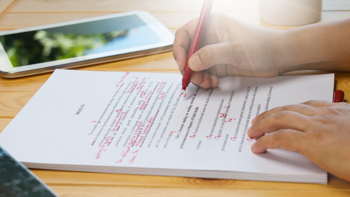A person correcting a printed text with a red pen