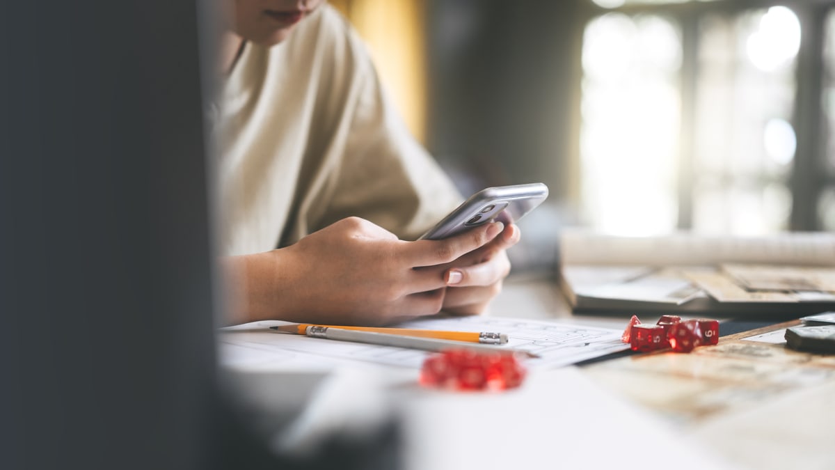 A person using a phone above tabletop role-playing notes and dice
